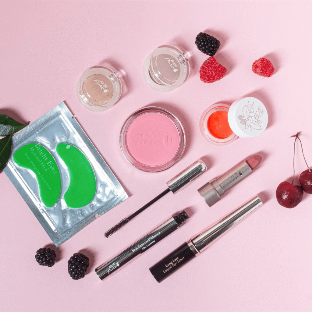 100% Pure non-toxic makeup flatlay featuring fruit-pigmented palettes, mascara, blush pot, lip balm, eye patches and berries