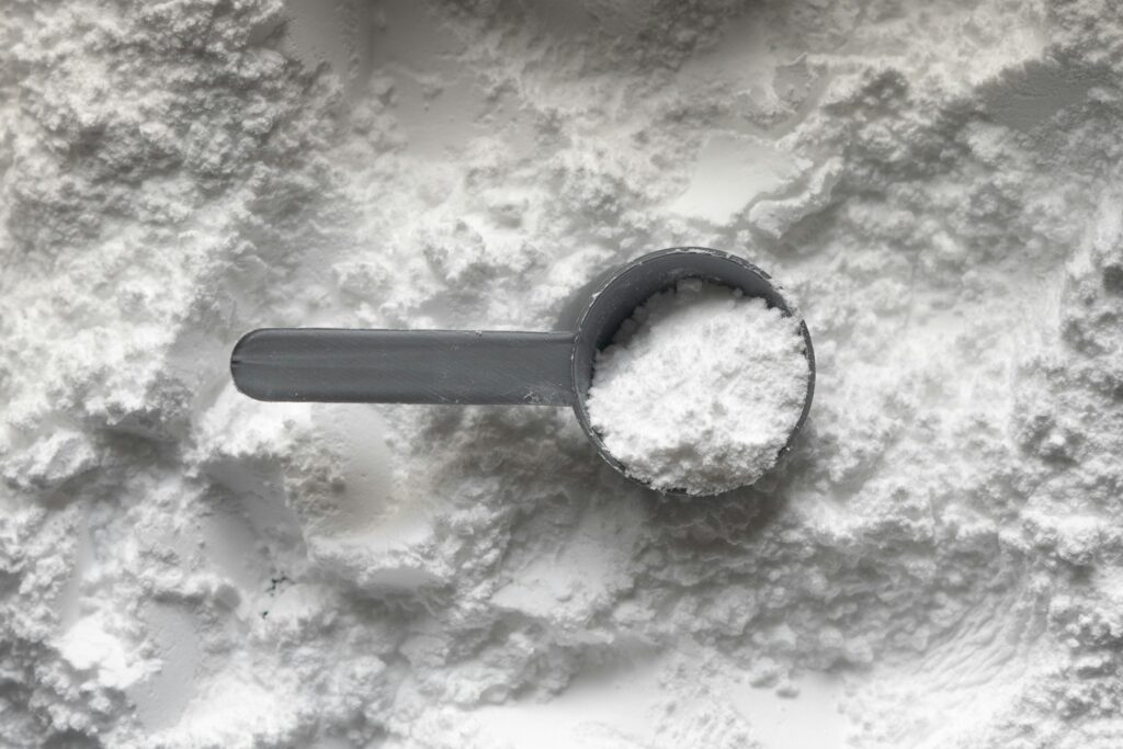 One scoop of white non-toxic protein powder. A sports supplement that is well studied and researched within the health and fitness industry, it helps to increase strength, muscle mass and endurance.