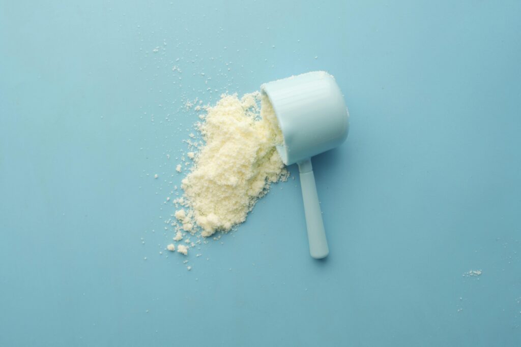 Photo of a white protein powder and a scoop lying on the blue background