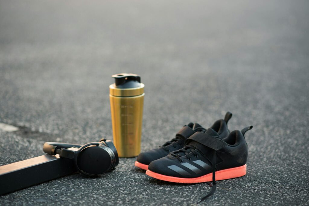 Contemporary sports equipment representing shaker bottle near wireless headset and stylish footwear on asphalt road