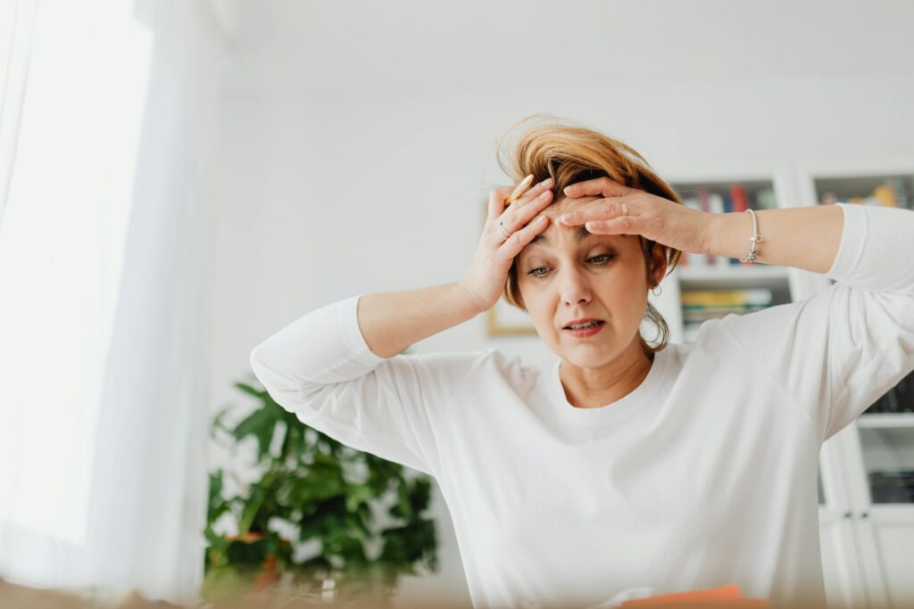 A worried woman indoors with hands on forehead, expressing stress.