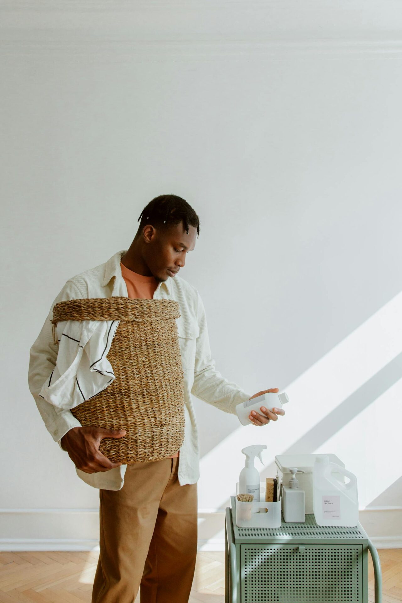 Adult man with laundry basket examines cleaning products in a bright minimalist room.