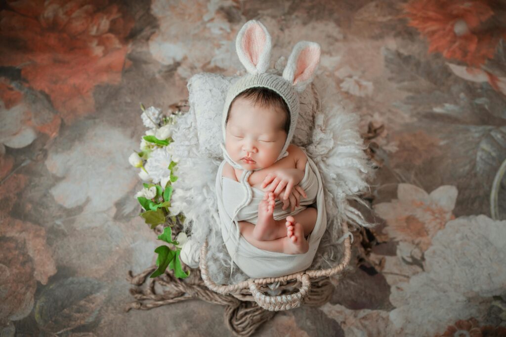 Charming newborn baby wearing easter bunny ears, peacefully sleeping in a cozy floral setting.