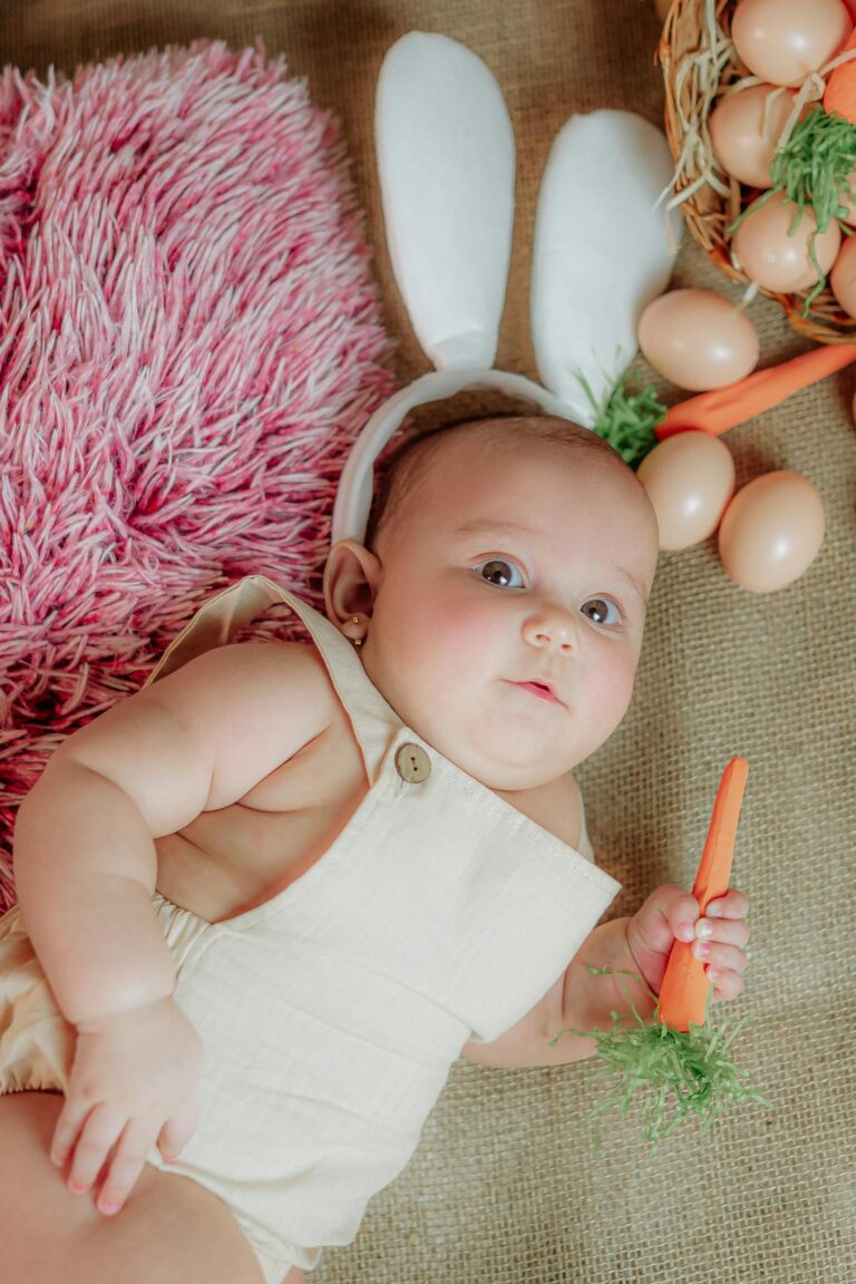 Cute baby with bunny ears holding a carrot, surrounded by eggs and pink fur, celebrating Easter.
