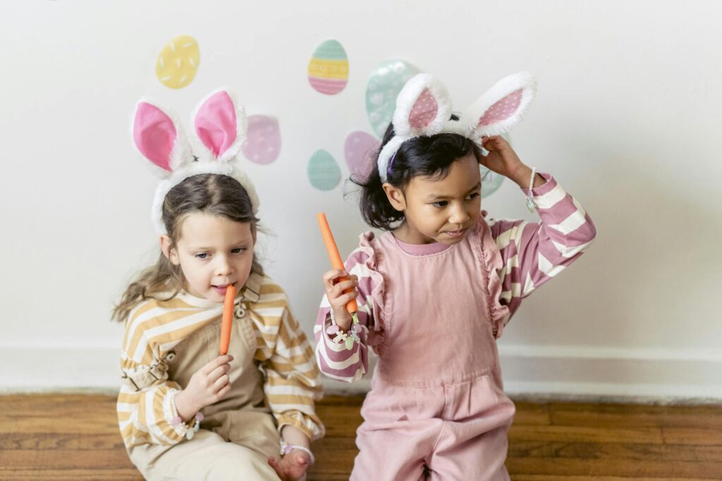 Two children wearing bunny ears and organic Easter outfits enjoy Easter treats indoors, adding festive fun.