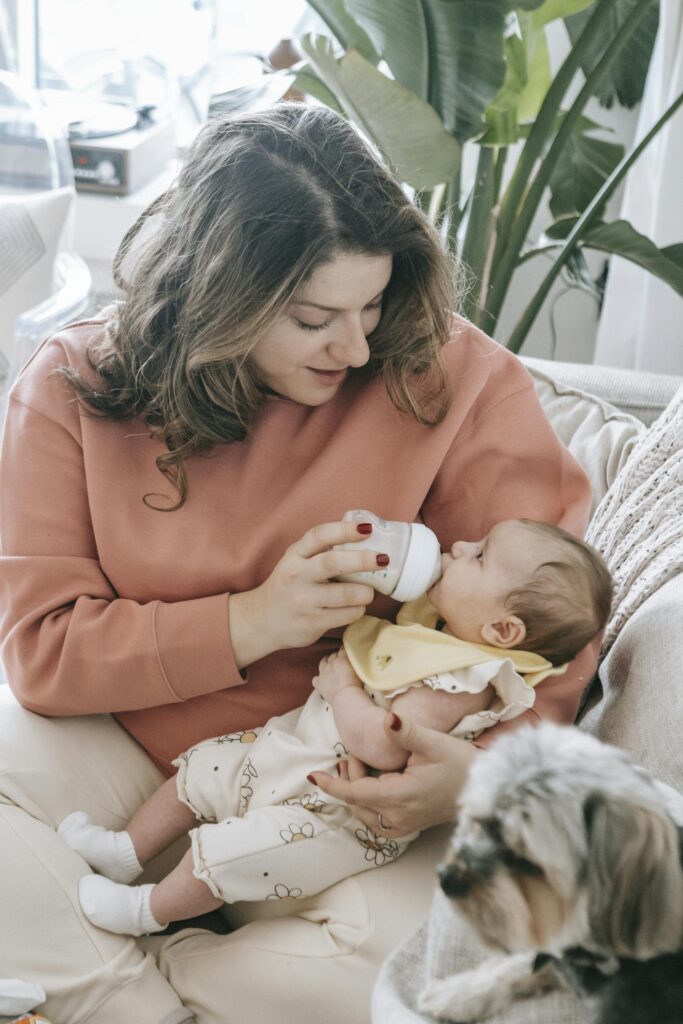 A mother lovingly feeds her baby a bottle while sitting on a cozy sofa indoors.