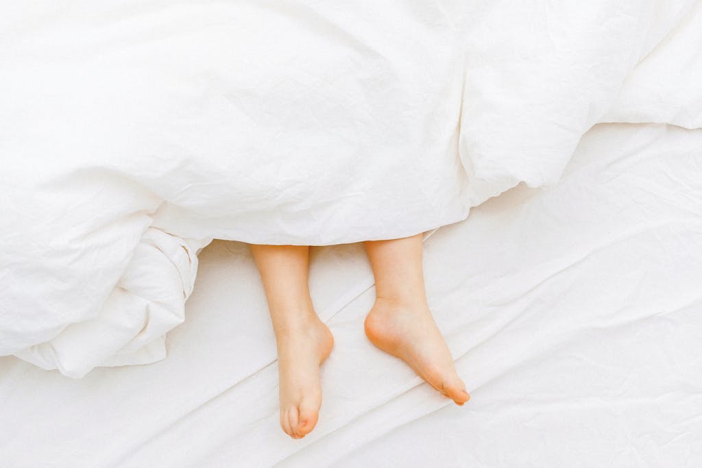 Organic white bedding with a child’s feet peeking from under the sheets, evoking a cozy, non-toxic sleep sanctuary