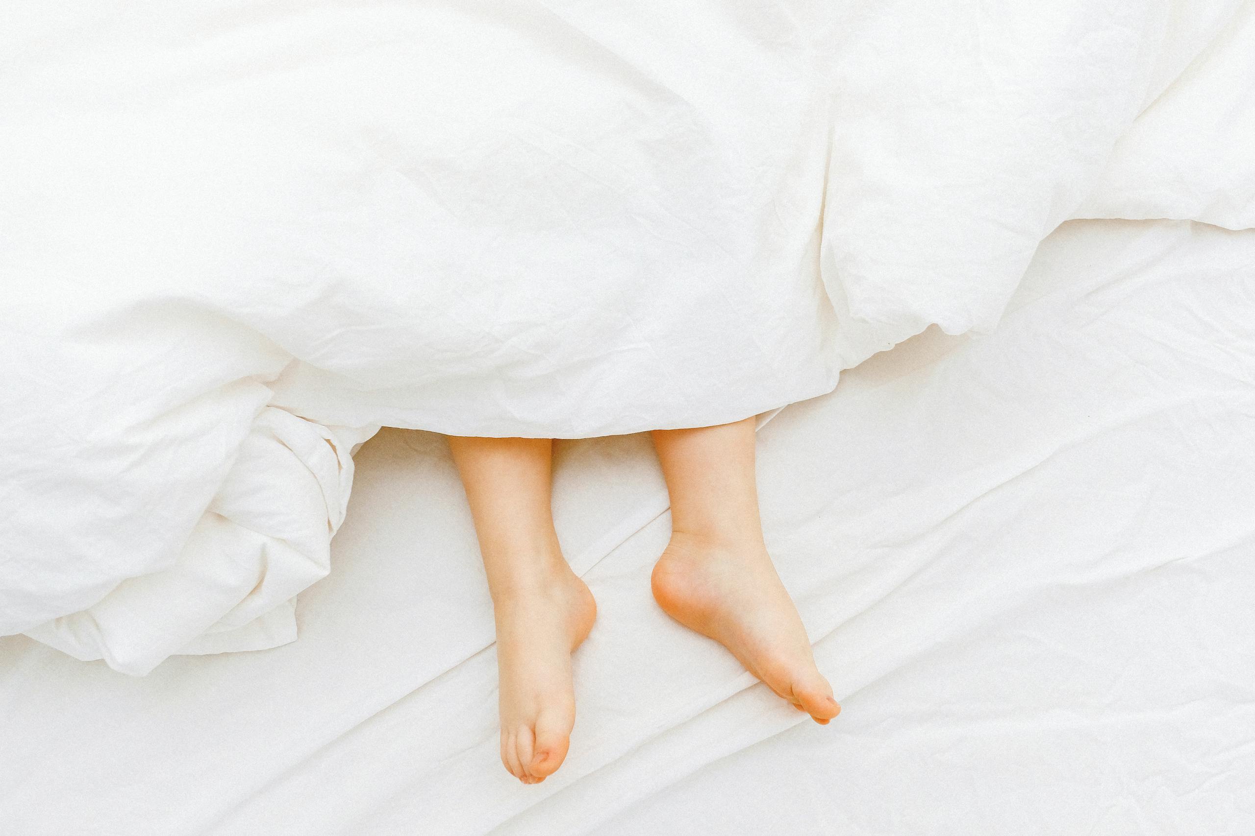 Child's feet under white sheets create a comforting and serene bedroom scene.