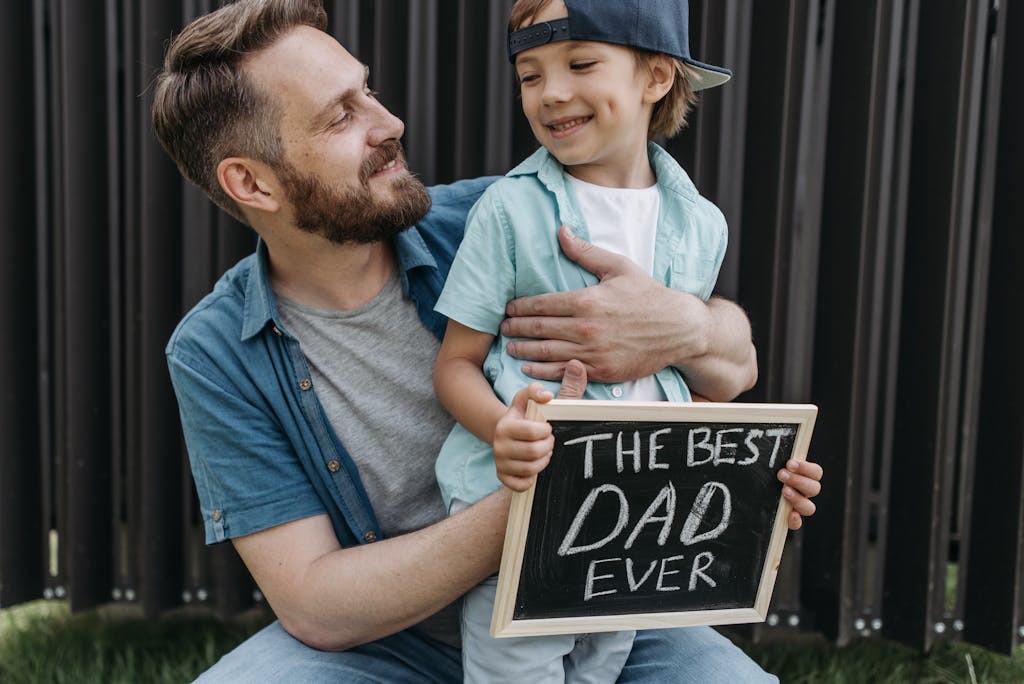 A father and son smiling outdoors holding a 'Best Dad Ever' sign.