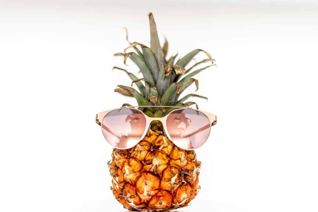 Playful pineapple wearing rose-gold sunglasses against a white background, evoking a non-toxic summer vibe for families