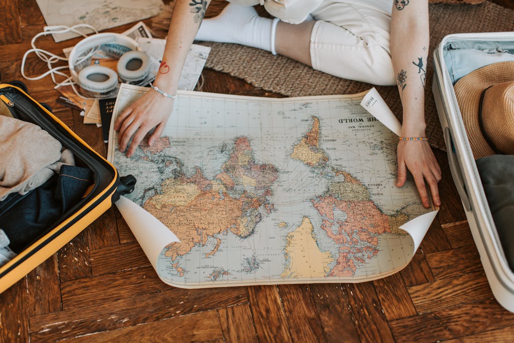 A traveler plans a journey, sitting on the floor with a world map and suitcase filled with non-toxic travel essentials.