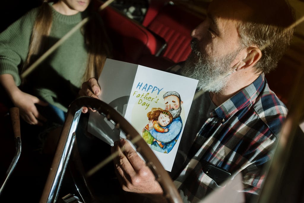 Father holding a Father's Day card inside a car, enjoying quality time with daughter.