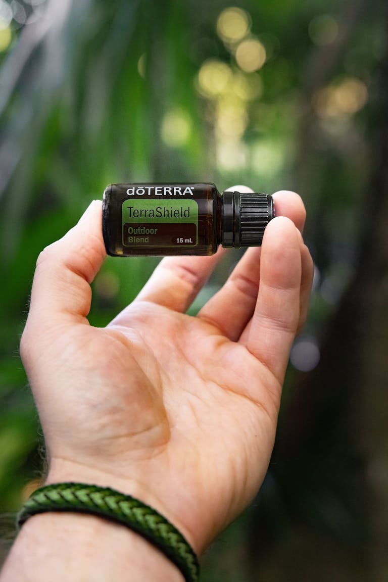 Person holding a bottle of doTERRA TerraShield essential oil non-toxic bug spray in a green outdoor setting.