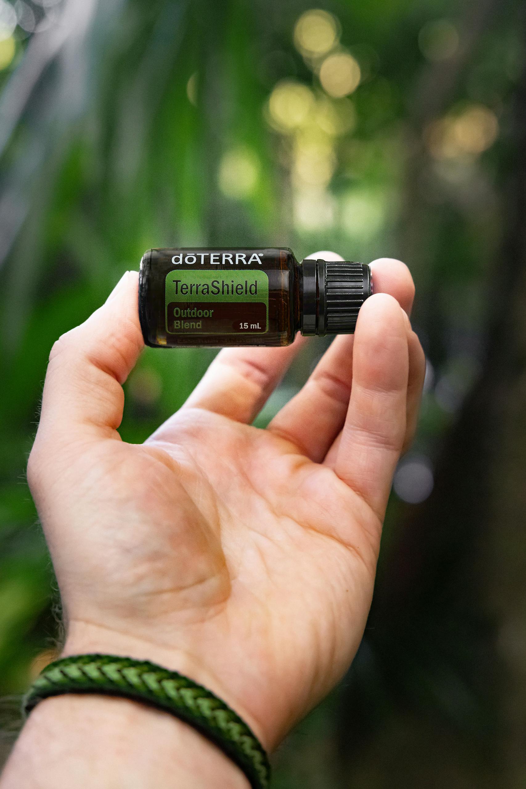 Person holding a bottle of doTERRA TerraShield essential oil non-toxic bug spray in a green outdoor setting.