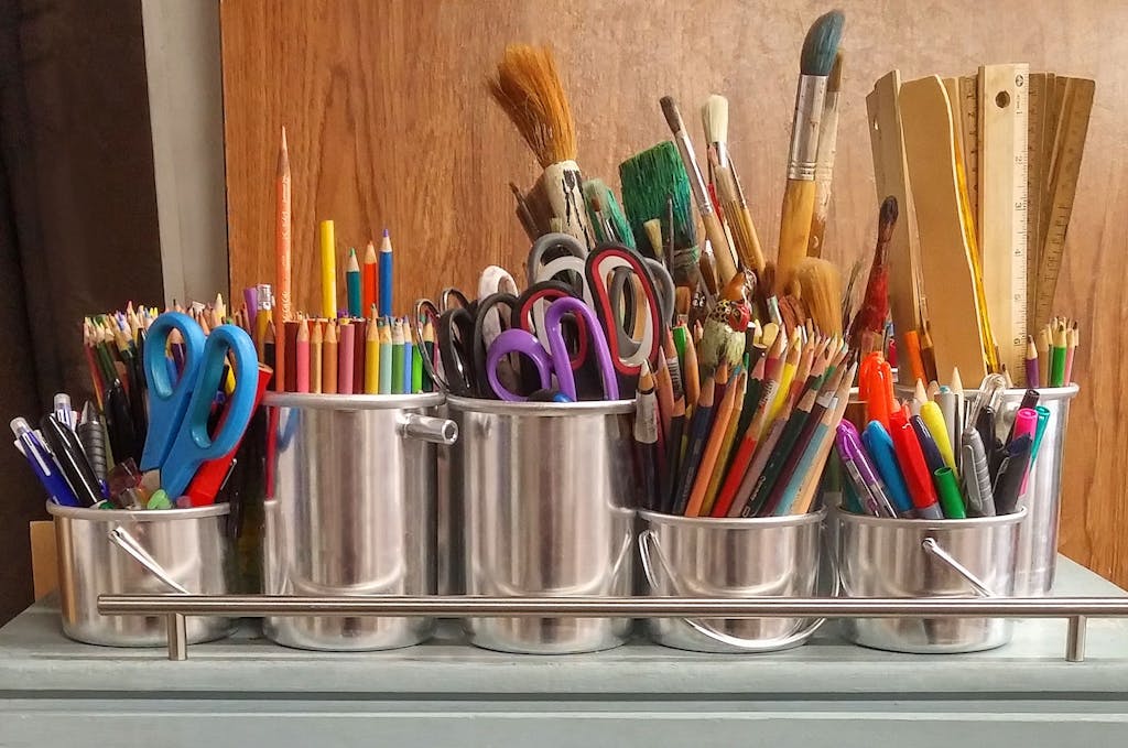 A diverse collection of non-toxic school supplies in metallic buckets on a wooden table.