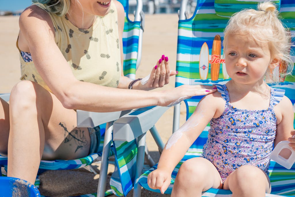 A mother applies non-toxic sunscreen to her young daughter on a sunny beach day.