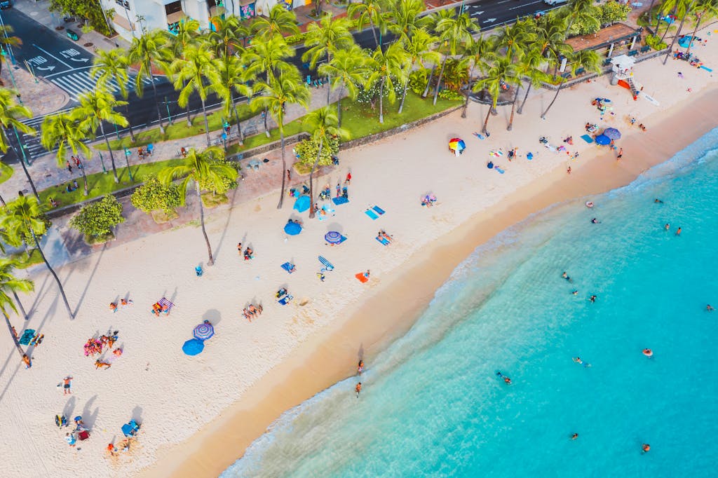 A stunning aerial shot of a bustling Hawaiian beach with clear waters and palm trees.