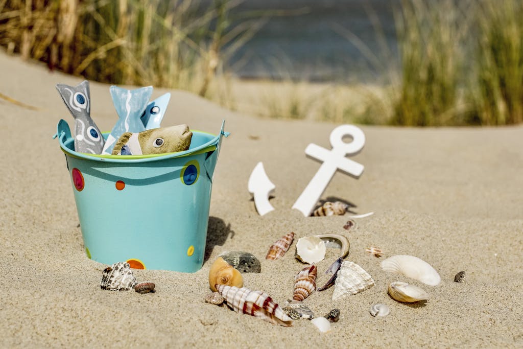 Decorative turquoise beach bucket with non-toxic sand toys and scattered seashells on golden sand for family beach days