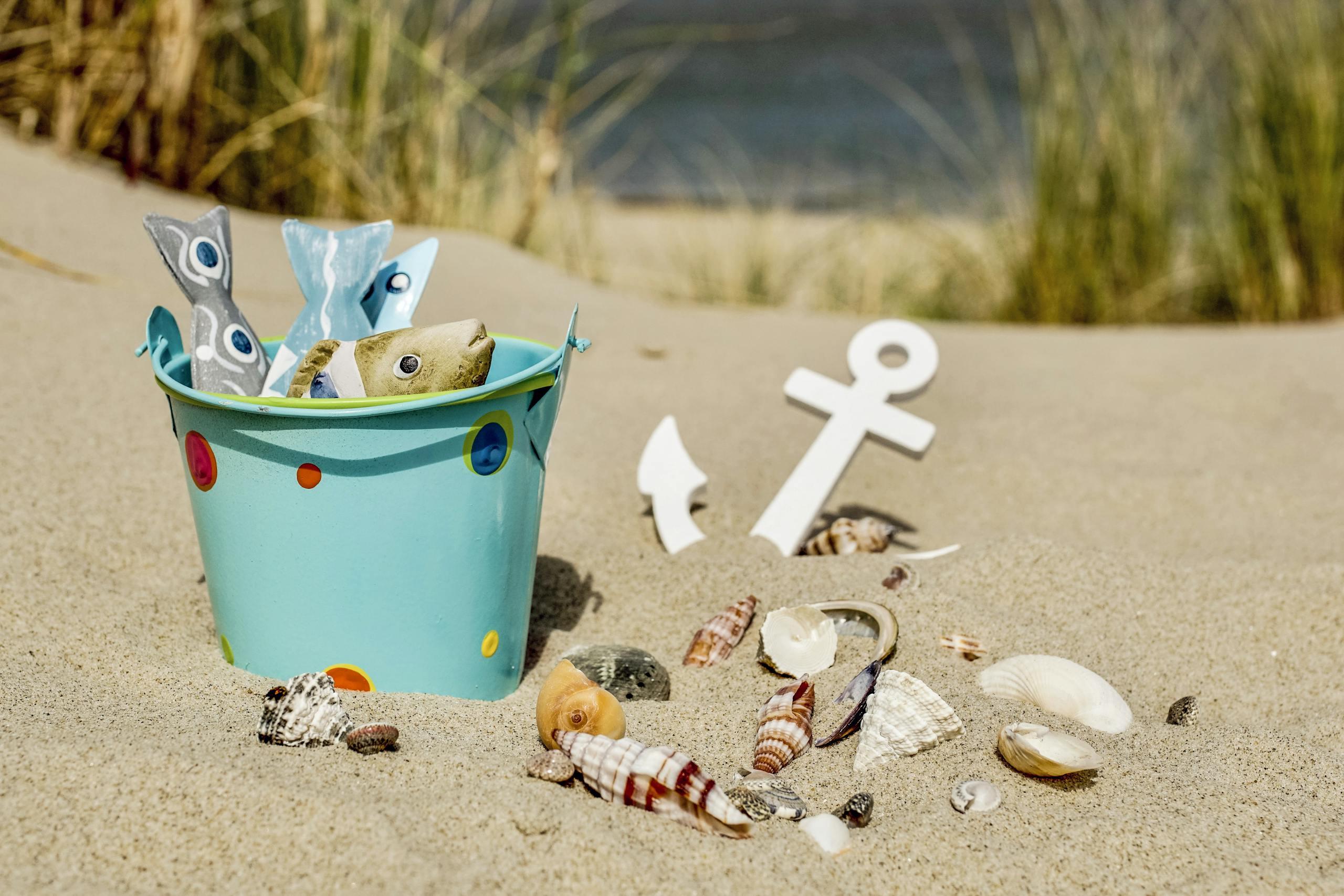 A vibrant beach scene featuring a decorative bucket filled with non-toxic beach gear and seashells on golden sand.