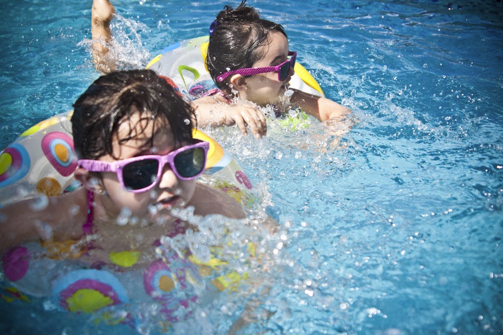Two young girls enjoying a playful day in a bright blue swimming pool with colorful non-toxic float rings.