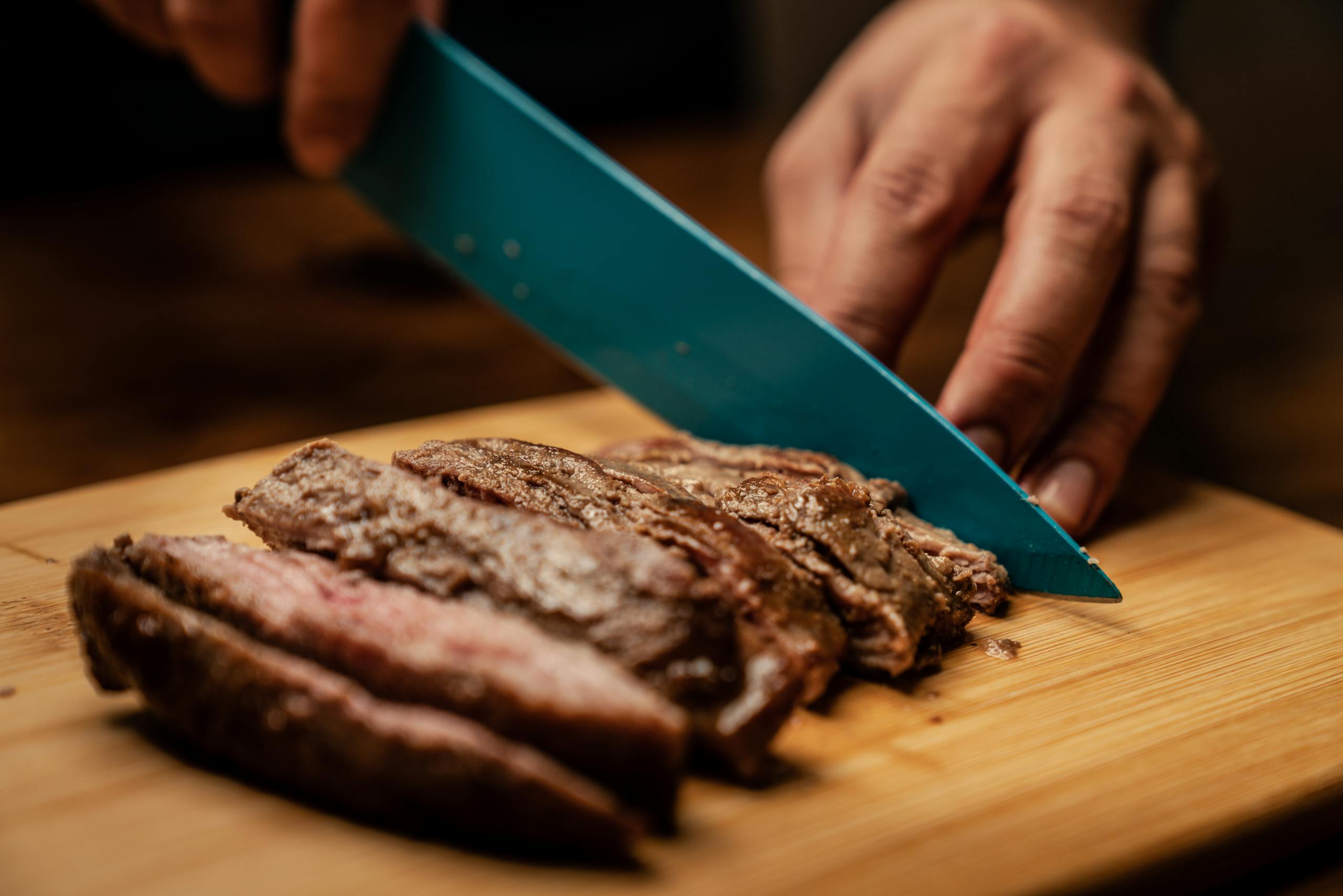 Hands slicing tender, juicy grilled steak on a non-toxic wood cutting board, showcasing a mouth-watering culinary scene.