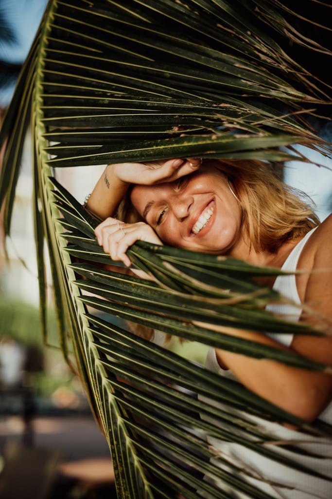 Smiling woman with blonde hair enjoying non-toxic living for beginners with palm leaves in foreground.