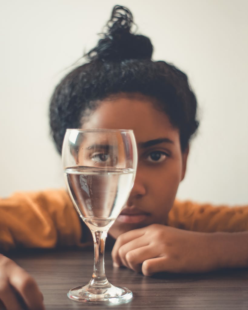 A young woman gazes through a wine glass filled with water from a non-toxic water filter, creating a unique visual effect.