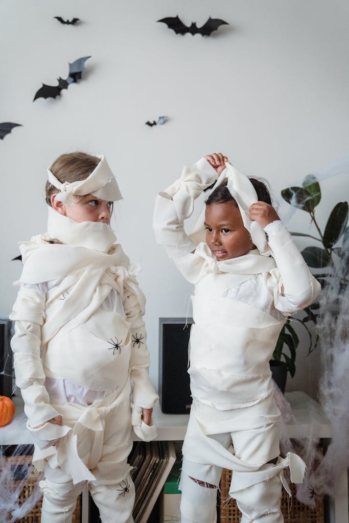 Kids in mummy costumes celebrating Halloween indoors with decorations.