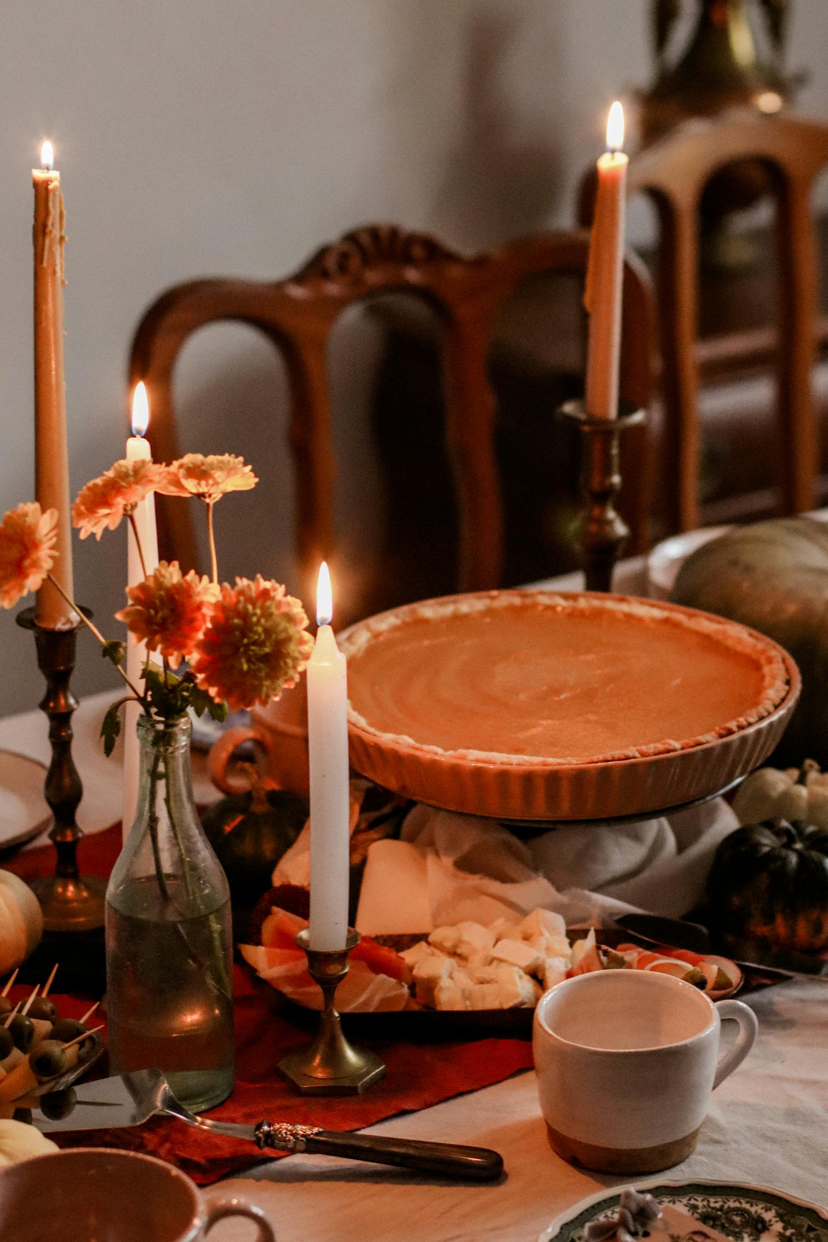 Warm autumn table setting with pumpkin pie, candles, and fall decor, creating a cozy ambiance.