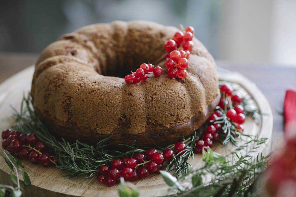 Palatable cake with ripe red berry bundle near pine sprigs on wooden tray during New Year holiday