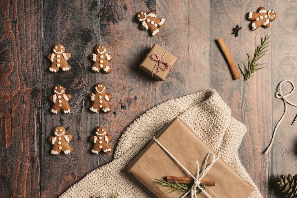 Top view of gingerbread cookies and wrapped gifts on a rustic wooden table, evoking Christmas warmth.