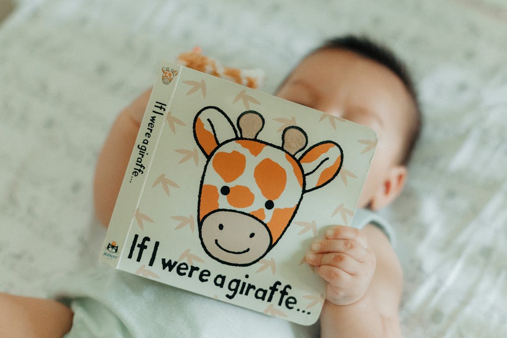 A cute baby holding a 'If I were a giraffe...' book while lying indoors, perfect for non-toxic baby registry themes.