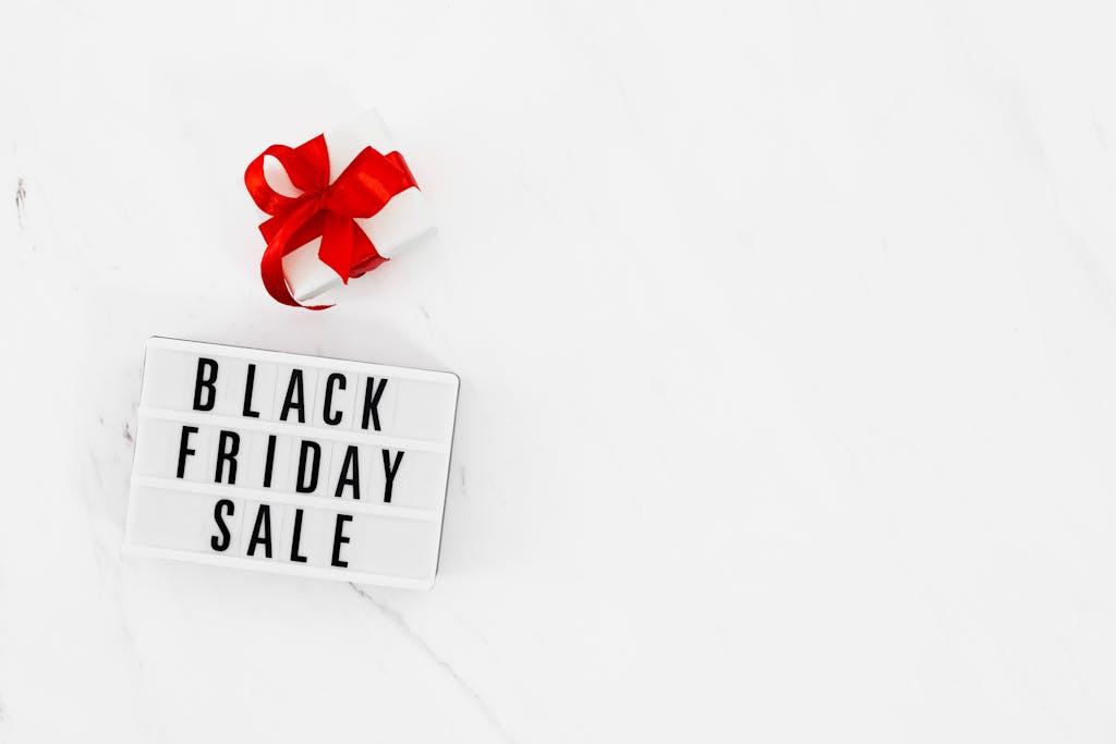 White background with Black Friday sale sign and red ribboned gift box for promoting non-toxic Black Friday deals and Cyber Monday sales.