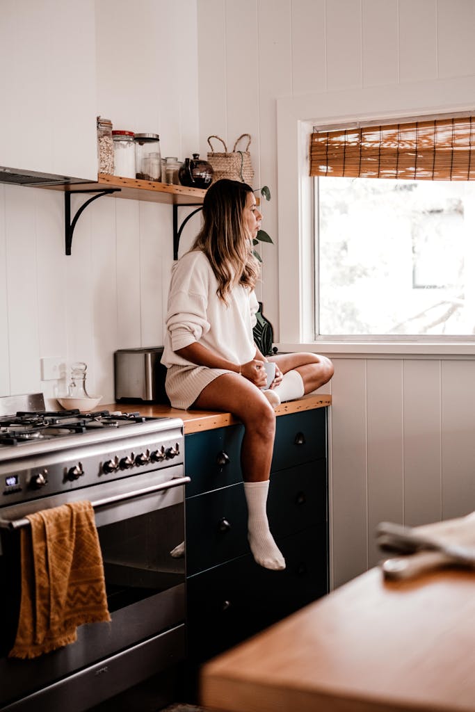 A woman sits on a kitchen counter by a window, creating a warm and inviting atmosphere.