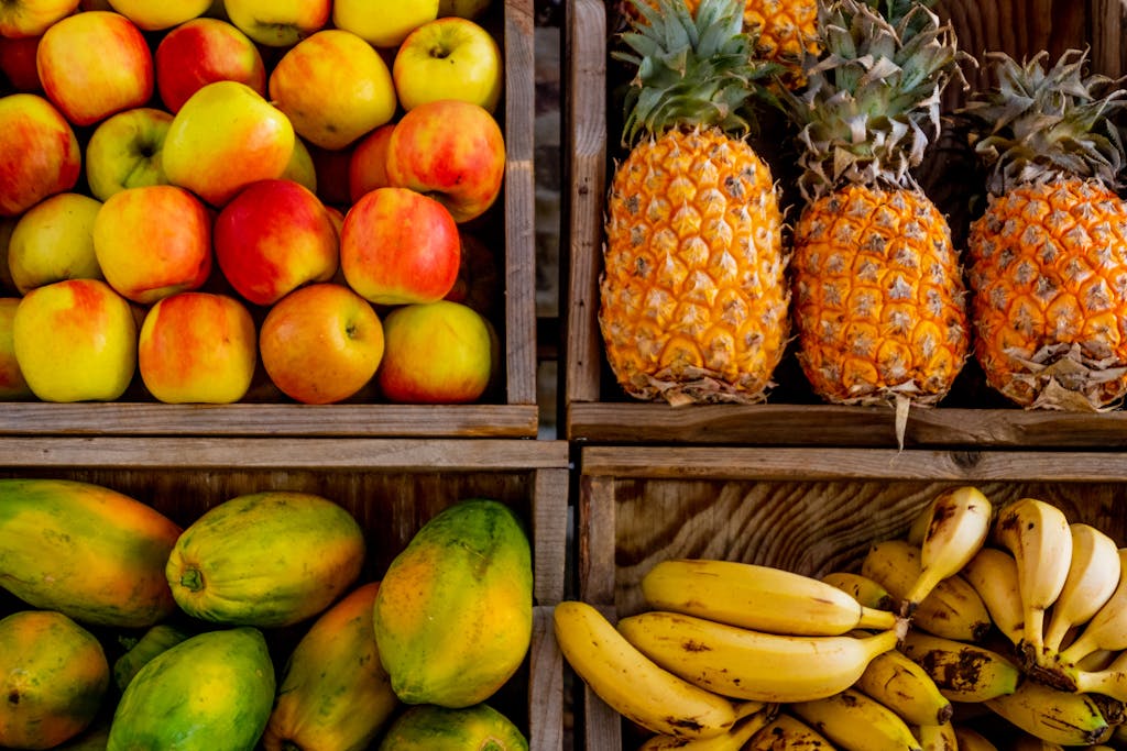 Colorful display of apples, pineapples, bananas, and papayas in wooden crates at a market, promoting non-toxic organic food shopping