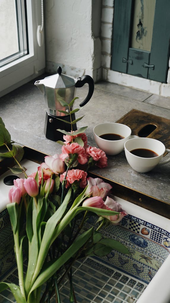 Cozy kitchen scene featuring coffee cups, flowers, and a moka pot for a warm atmosphere.