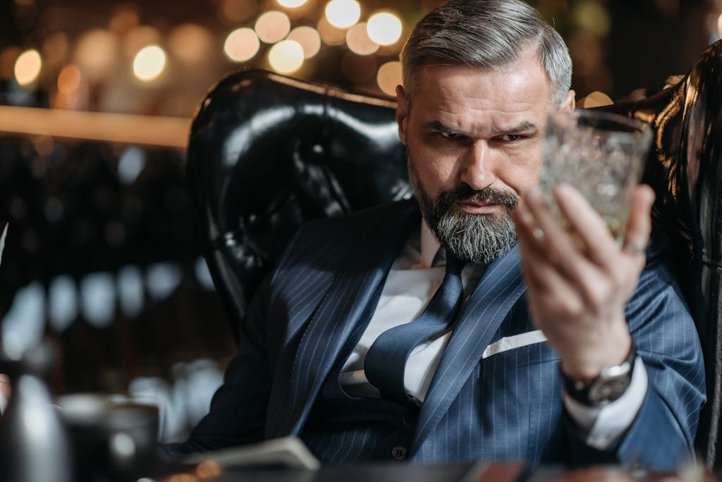 Mature businessman in a suit inspecting a lead-free glass of whiskey with focus indoors.