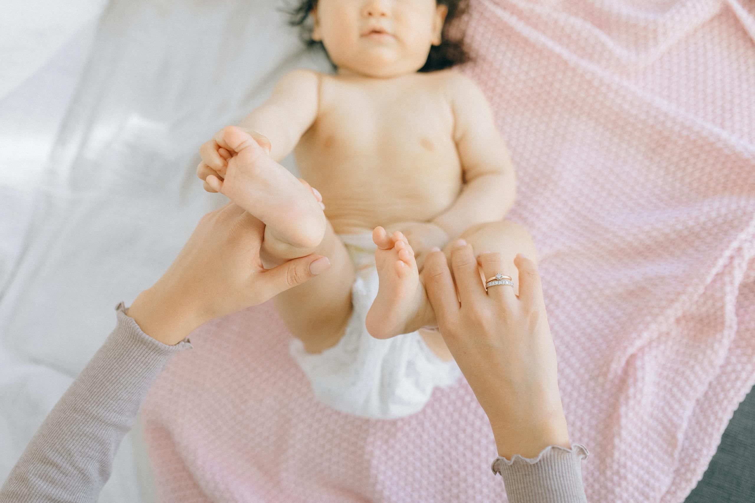A parent holds a baby's feet on a pink blanket, capturing a tender moment.