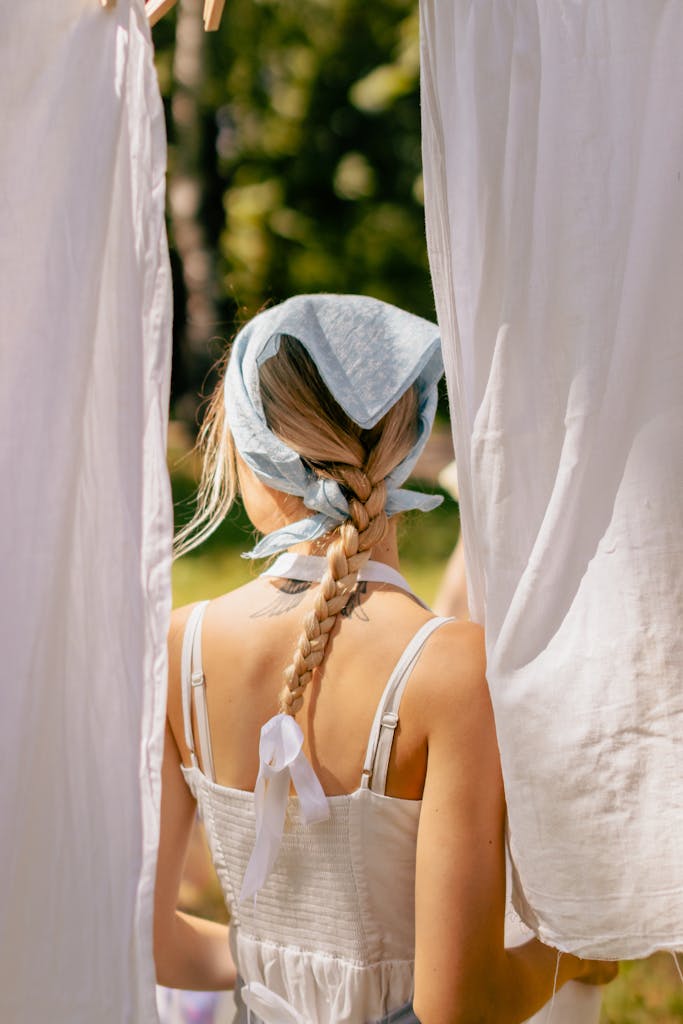 Back view of a woman with braided hair in a summer dress standing outdoors between hanging non-toxic laundry.