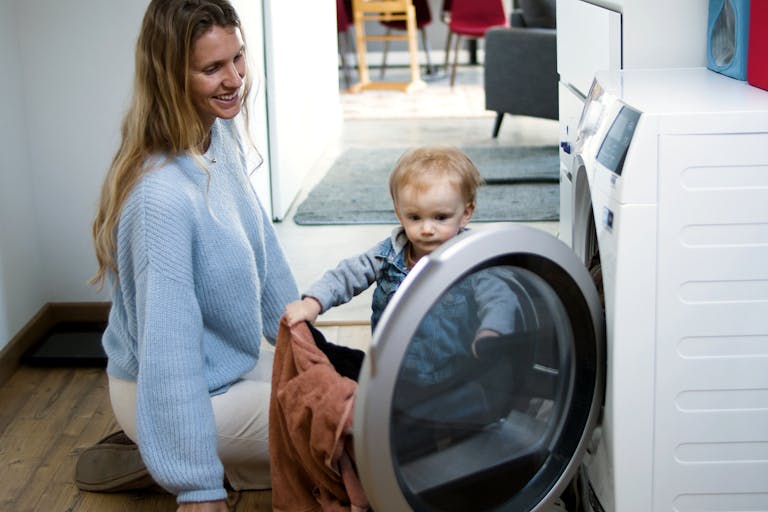 Mother and toddler joyfully doing laundry together, fostering family bonding at home.