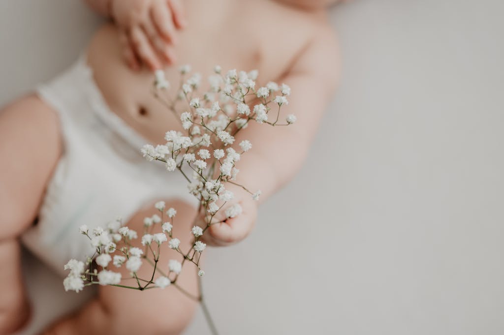 Portrait of a baby in a non-toxic diaper delicately holding white flowers, emphasizing innocence.