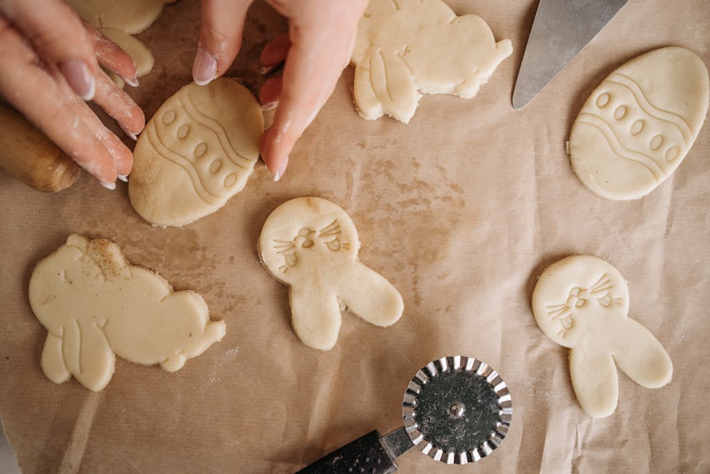 Hands preparing Easter-themed cookies with bunny shapes on baking paper.