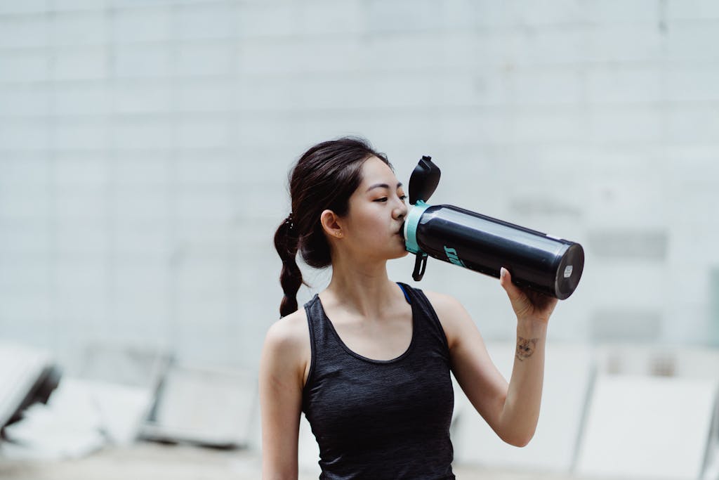 Young woman in workout attire drinks from a plastic free shaker bottle, promoting healthy lifestyle.