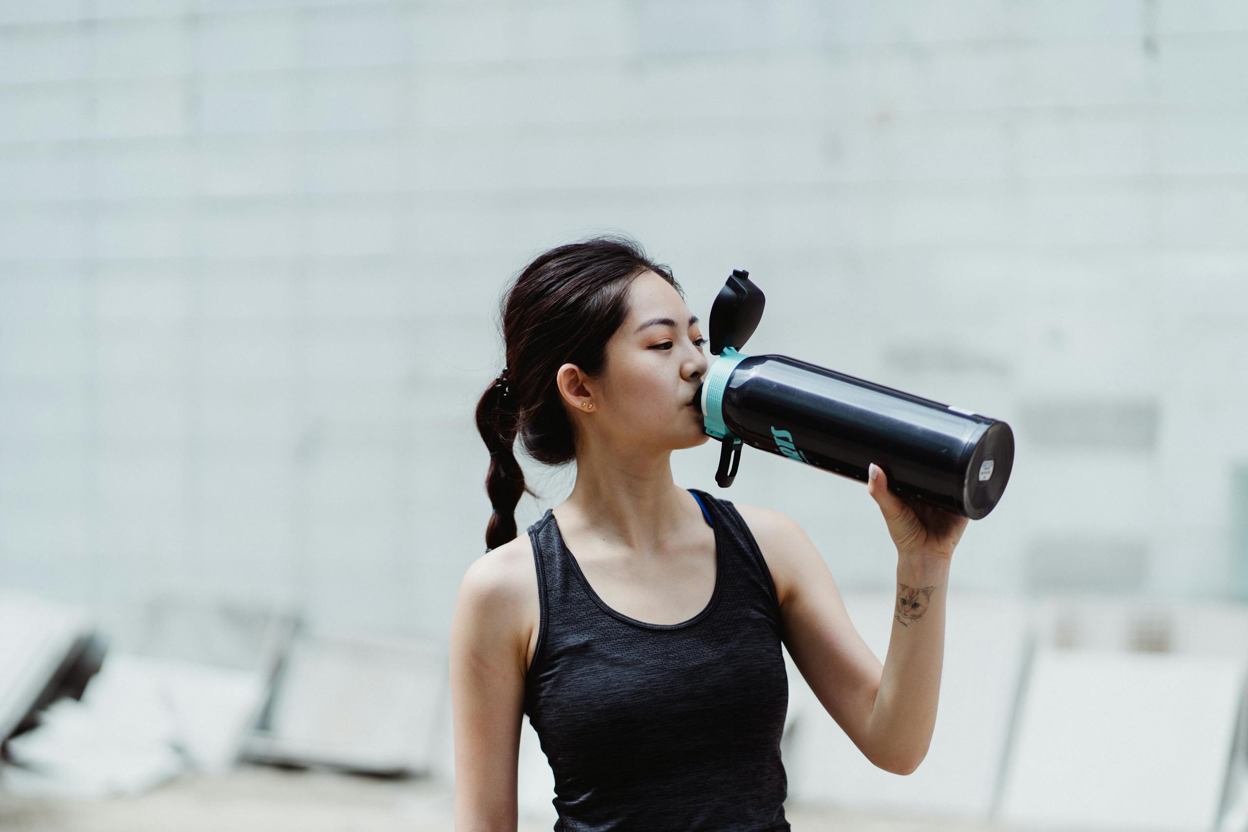 Young woman in workout attire drinks from a plastic free shaker bottle, promoting healthy lifestyle.