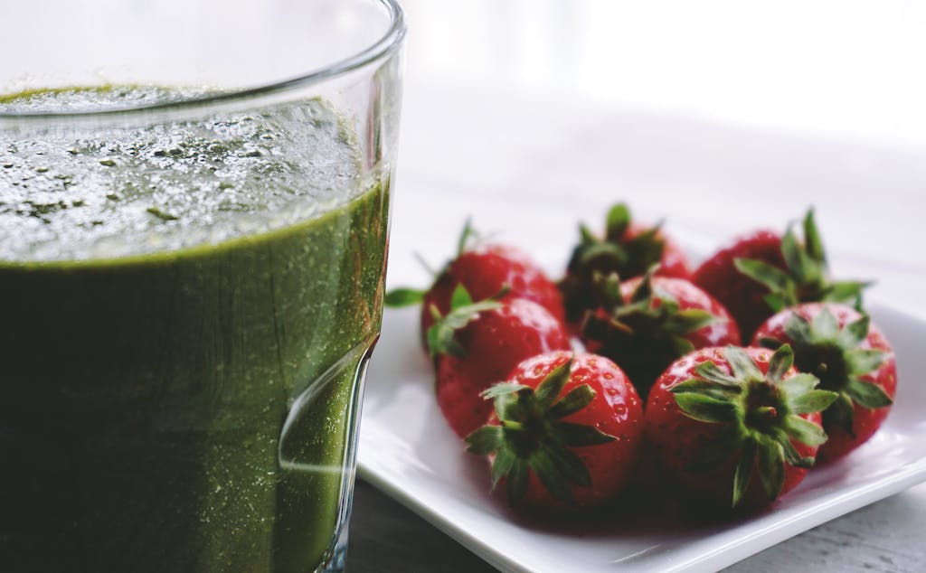 Close-up of a green protein smoothie and fresh strawberries on a white saucer.
