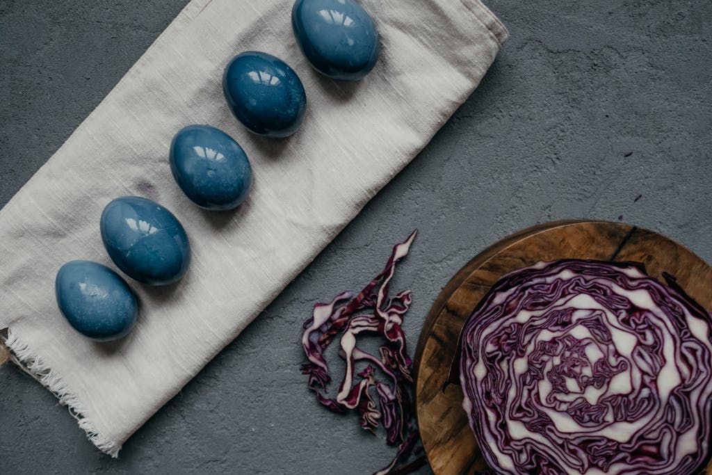 Five blue dyed Easter eggs on cloth with red cabbage on wooden board, artistic presentation.