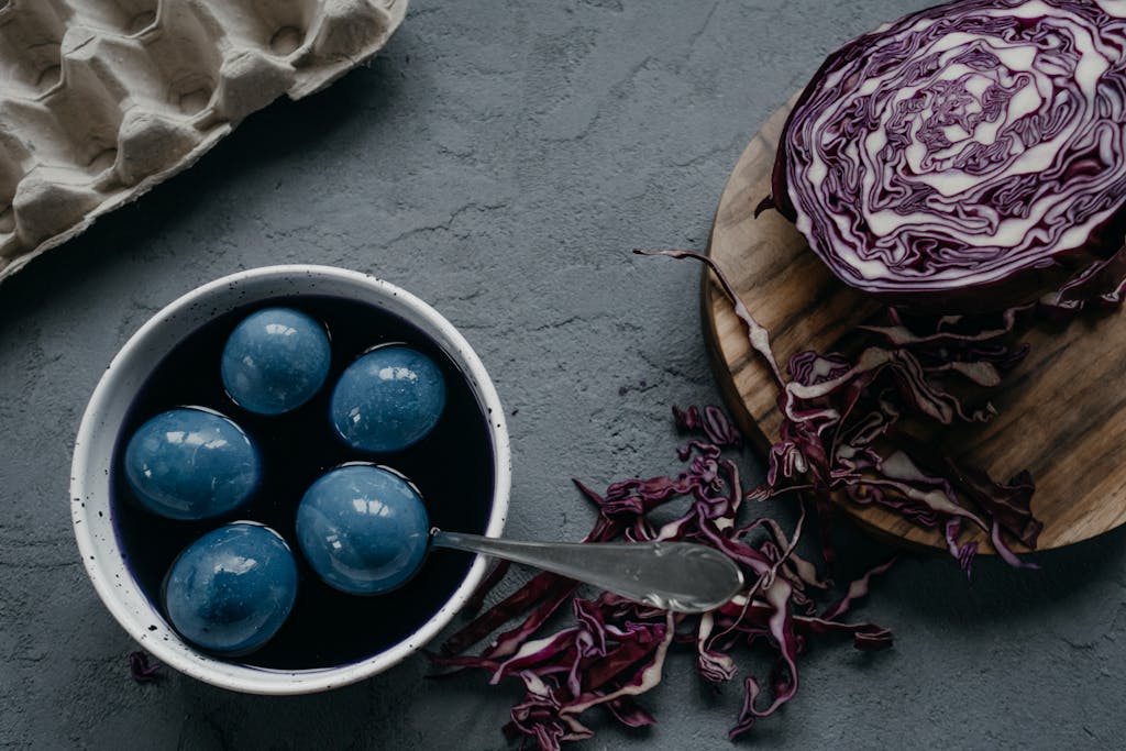 Naturally dyed blue Easter eggs soaking in red cabbage dye with sliced cabbage and an egg carton in a rustic setting