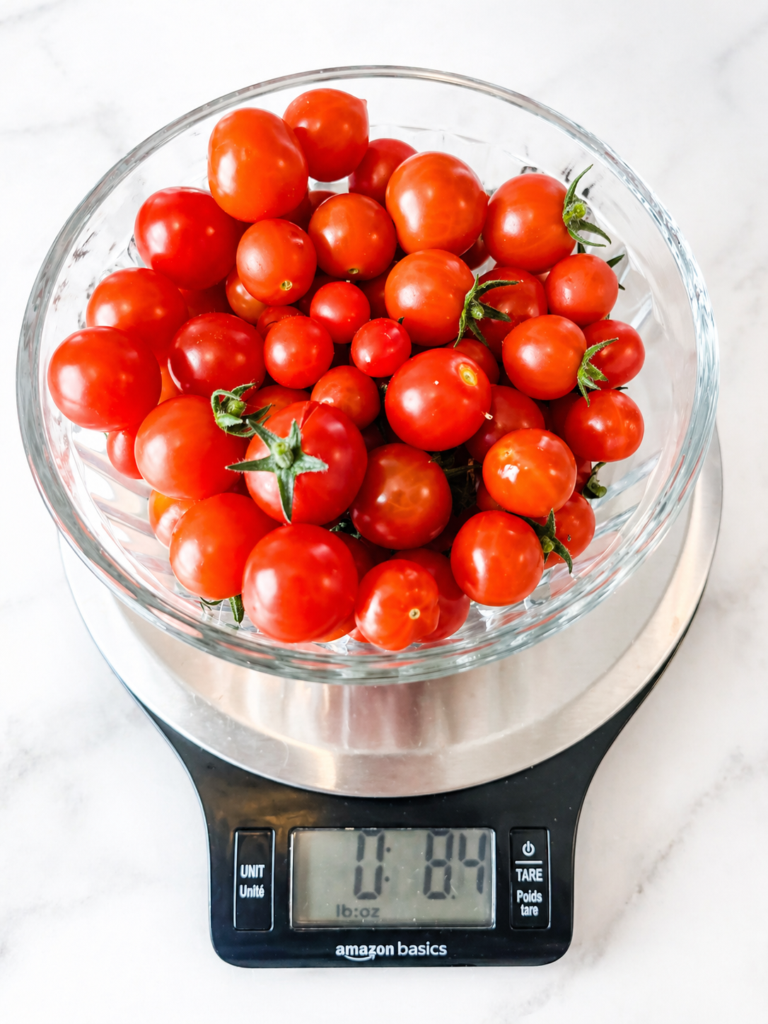 homegrown pesticide-free cherry tomatoes collected in a glass bowl sit on a scale, showing a harvest of over 8 ounces