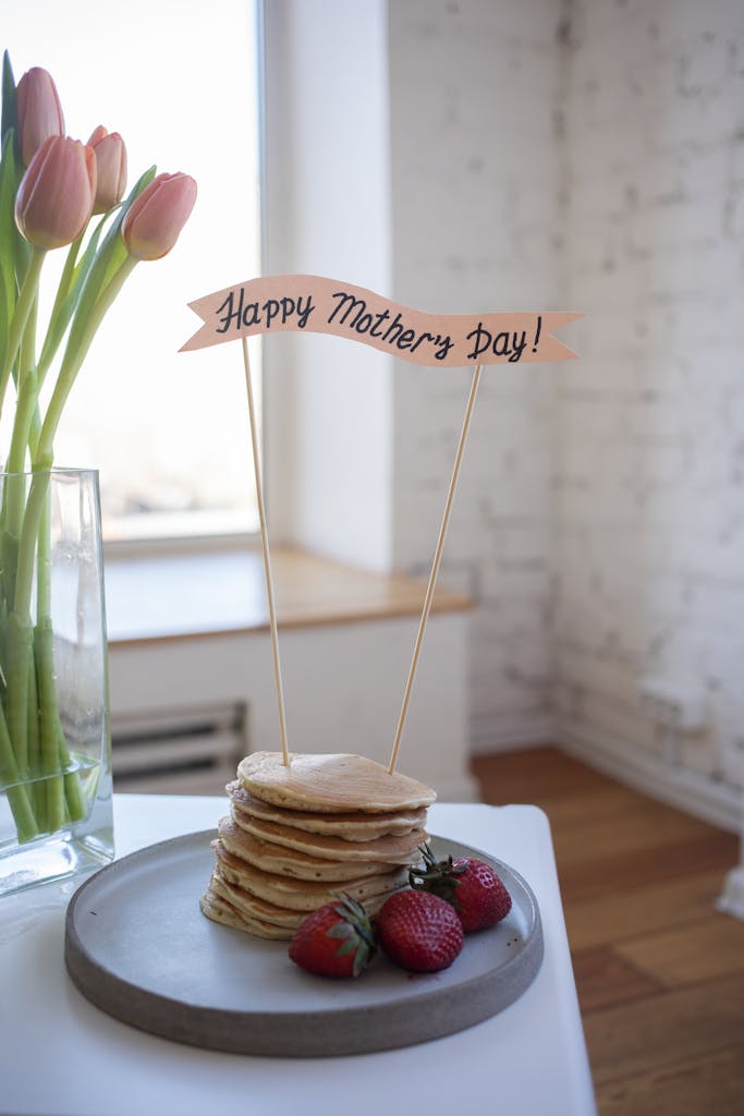 A stack of pancakes with strawberries and tulips, celebrating Mother's Day with a festive banner.