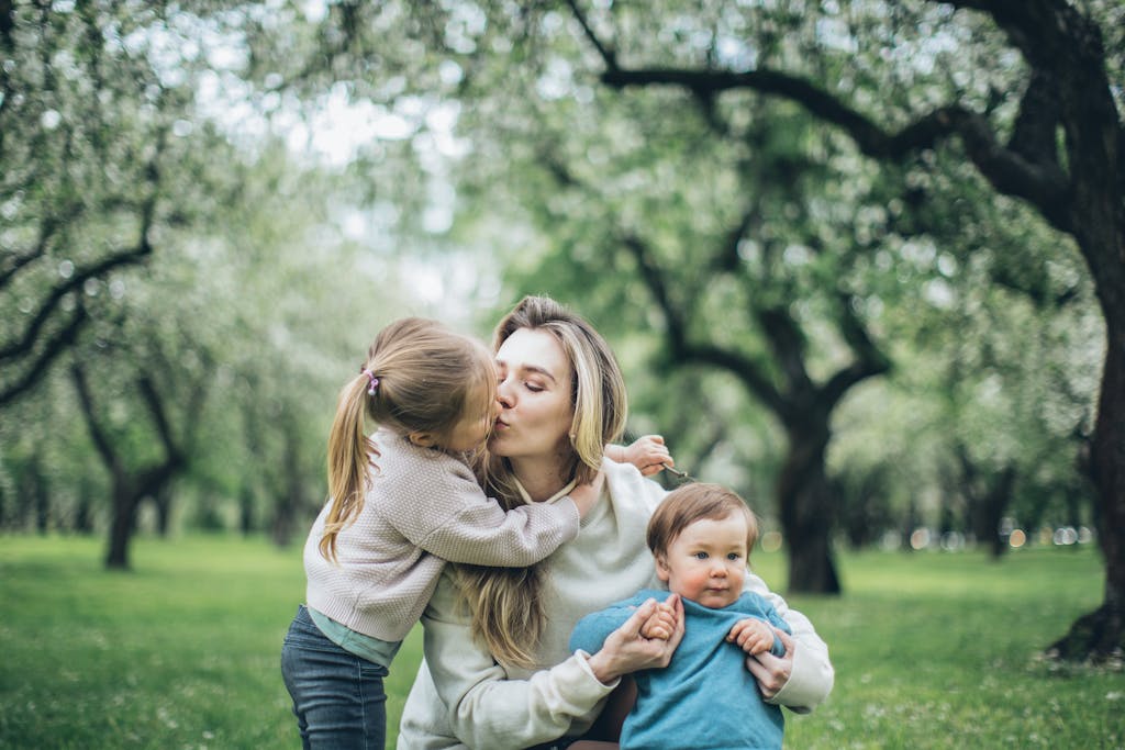Mother kissing and holding her two young children in a blooming spring park for non-toxic Mother’s Day gift feature